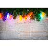 Multicolored Christmas lights on spruce branch with wooden background