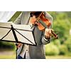 Male violinist playing his instrument and reading a music sheet during an outdoor summer wedding ceremony (shallow DOF; color toned image)