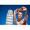 Gorgeous young woman taking a selfie with her smart phone in front of the Leaning Tower of Pisa, Tuscany, Italy (shallow DOF)