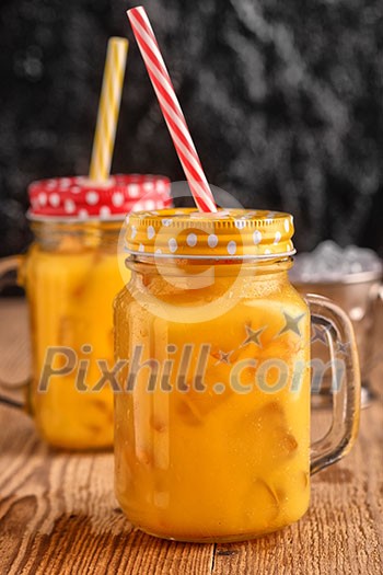 Fresh orange juice with ice in a mason jar on wooden table Fresh orange juice with ice in a mason jar on wooden table