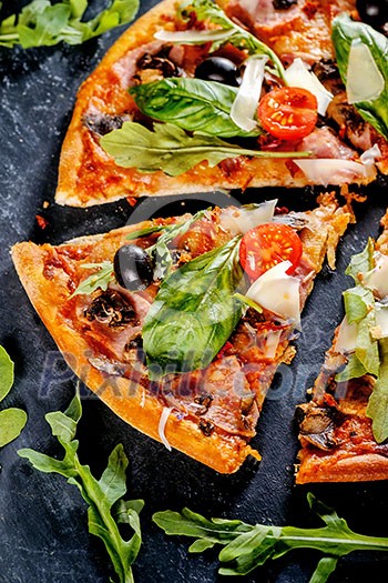 Cut into slices delicious fresh pizza with mushrooms, tomatoes, basil and bacon on a dark background. Pizza on the black table. Cut into slices delicious fresh pizza with mushrooms, tomatoes, basil and bacon on a dark background. Pizza on the black table.