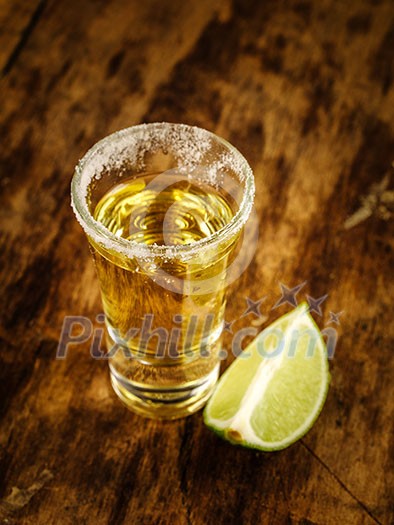 Gold tequila shot with lime on wooden background, selective focus. Gold tequila shot with lime on wooden background, selective focus.