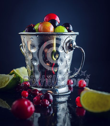 Small metal pail with different berries on dark table. Shallow depth of field. Rustic style. Toned. Small metal pail with different berries on dark table. Shallow depth of field. Rustic style. Toned.