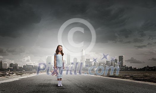 Cute girl wearing pajamas with toy bear in hand standing on road Cute girl wearing pajamas with toy bear in hand standing on road