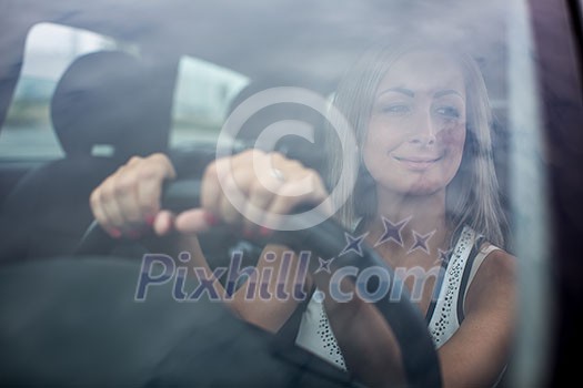 Woman driving a car - female driver at a wheel of a modern car, looking happy, smiling with a relaxed smile (shallow DOF; color toned image) Woman driving a car - female driver at a wheel of a modern car, looking happy, smiling with a relaxed smile (shallow DOF; color toned image)