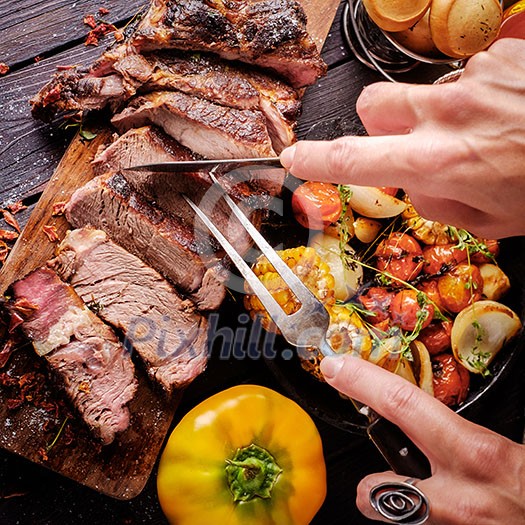 Grilled steak sliced on a cutting board. Entrecote with vegetables on a wooden background. Woman slicing a grilled beef stead. Grilled steak sliced on a cutting board. Entrecote with vegetables on a wooden background. Woman slicing a grilled beef stead.