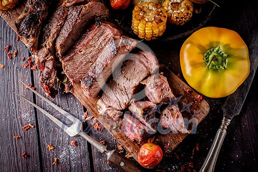 Grilled steak sliced on a cutting board. Entrecote with vegetables on a wooden background. Grilled steak sliced on a cutting board. Entrecote with vegetables on a wooden background.