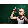 Cute school girl in glasses standing at blackboard