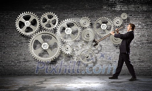 Young businessman fixing gears mechanism with wrench Young businessman fixing gears mechanism with wrench