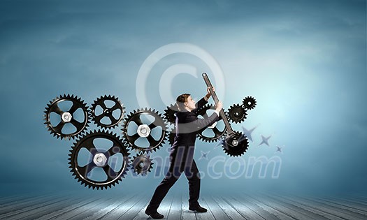 Young businessman fixing gears mechanism with wrench Young businessman fixing gears mechanism with wrench
