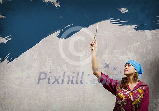 Young woman in headscarf painting wall with brush Young woman in headscarf painting wall with brush