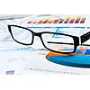 Eye glasses lying on papers with graphs and diagrams