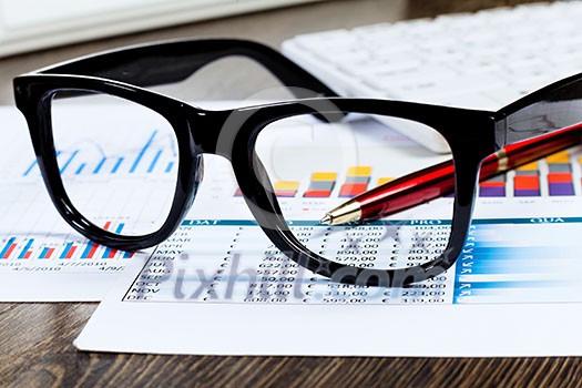 Eye glasses lying on papers with graphs and diagrams Eye glasses lying on papers with graphs and diagrams