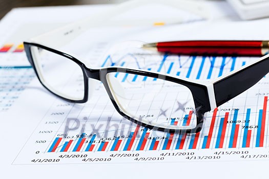 Eye glasses lying on papers with graphs and diagrams Eye glasses lying on papers with graphs and diagrams