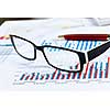 Eye glasses lying on papers with graphs and diagrams