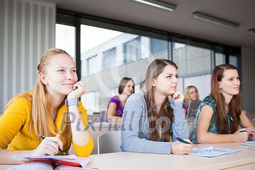 Students in classroom - young pretty female college student sitting in a classroom full of students during class (color toned image; shallow DOF) Students in classroom - young pretty female college student sitting in a classroom full of students during class (color toned image; shallow DOF)