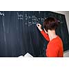 Pretty, young college student writing on the chalkboard/blackboard during a math class (color toned image)