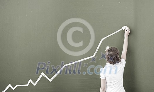 Cute little girl standing with back and drawing on blackboard Cute little girl standing with back and drawing on blackboard