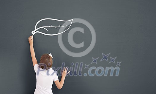 Cute little girl standing with back and drawing on blackboard Cute little girl standing with back and drawing on blackboard