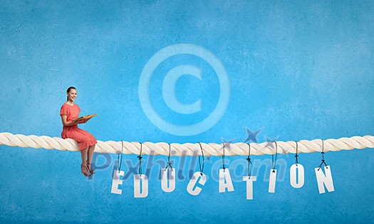 Young woman in red dress sitting on rope with book in hand Young woman in red dress sitting on rope with book in hand