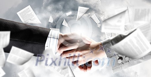 Close up of business handshake with papers at background Close up of business handshake with papers at background