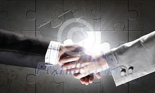 Close up of business handshake with puzzle elements at background Close up of business handshake with puzzle elements at background