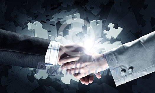 Close up of business handshake with puzzle elements at background Close up of business handshake with puzzle elements at background