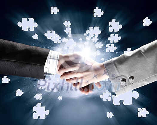 Close up of business handshake with puzzle elements at background Close up of business handshake with puzzle elements at background