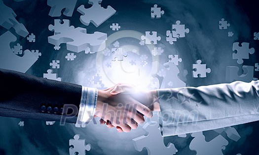 Close up of business handshake with puzzle elements at background Close up of business handshake with puzzle elements at background
