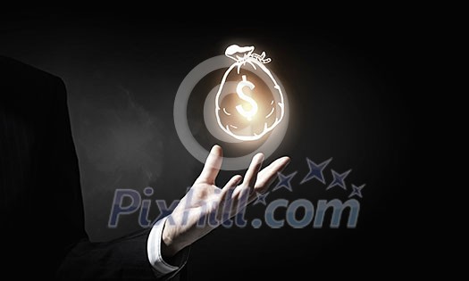 Hand of businessman holding money bag symbol on dark background Hand of businessman holding money bag symbol on dark background
