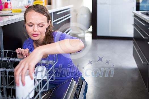 Pretty, young woman in her modern and well equiped kitchen putting cups into the dishwasher - an appliance that helps her keep the home tidy Pretty, young woman in her modern and well equiped kitchen putting cups into the dishwasher - an appliance that helps her keep the home tidy