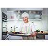 Senior woman cooking in the kitchen - eating and cooking healthy for her family; putting some potates in the oven, enjoying active retirement (shallow DOF; color toned image)