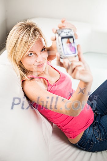 Pretty young woman taking a picture of herself while sitting on a sofa in her new apartment Pretty young woman taking a picture of herself while sitting on a sofa in her new apartment