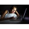 Pretty, young woman using her laptop computer in bed (color toned image; shallow DOF)