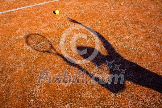 shadow of a tennis player in action on a tennis court (conceptual image with a tennis ball lying on the court and the shadow of the player positioned in a way he seems to be playing it)