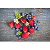 Fresh small wild strawberries and blueberries on old blue wooden background