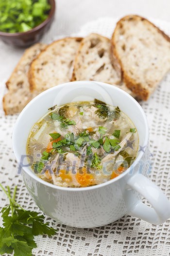 Cup of hot chicken rice soup served with bread and parsley on crochet tablecloth Cup of hot chicken rice soup served with bread and parsley on crochet tablecloth