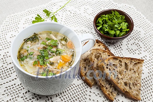 Cup of hot chicken rice soup served with bread and parsley on crochet tablecloth Cup of hot chicken rice soup served with bread and parsley on crochet tablecloth