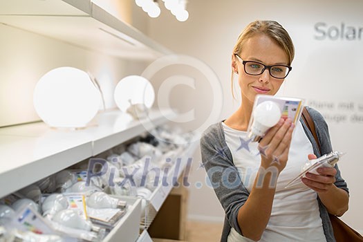 Energy efficient lighting choice: Pretty, young woman holding and choosing a LED diode light bulb for her lamp in DIY department store Energy efficient lighting choice: Pretty, young woman holding and choosing a LED diode light bulb for her lamp in DIY department store