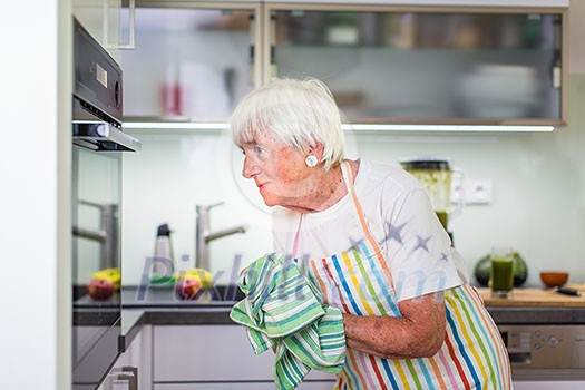 Senior woman cooking in the kitchen - eating and cooking healthy for her family; putting some potates in the oven, enjoying active retirement (shallow DOF; color toned image) Senior woman cooking in the kitchen - eating and cooking healthy for her family; putting some potates in the oven, enjoying active retirement (shallow DOF; color toned image)