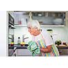 Senior woman cooking in the kitchen - eating and cooking healthy for her family; putting some potates in the oven, enjoying active retirement (shallow DOF; color toned image)
