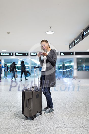 Young female passenger at the airport, using her tablet computer while waiting for her flight (color toned image) Young female passenger at the airport, using her tablet computer while waiting for her flight (color toned image)