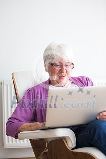 Portrait of a senior woman at home - Laughing at something on her laptop computer, sitting in her favorite chair, enjoying retirement Portrait of a senior woman at home - Laughing at something on her laptop computer, sitting in her favorite chair, enjoying retirement