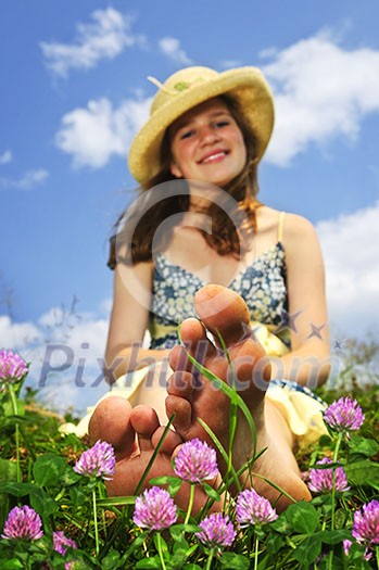 Young teenage girl sitting on summer meadow amid wildflowers in straw hat Young teenage girl sitting on summer meadow amid wildflowers in straw hat