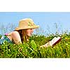 Young teenage girl reading book in summer meadow with straw hat