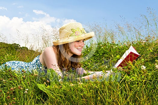 Young teenage girl reading book in summer meadow with straw hat Young teenage girl reading book in summer meadow with straw hat