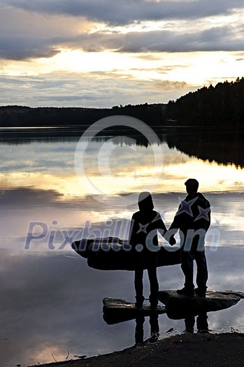 Sun setting over tranquil lake with people watching in silhouette Sun setting over tranquil lake with people watching in silhouette