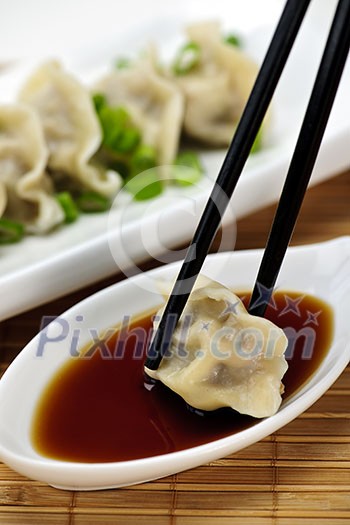 Dumpling being dipped in soy sauce with chopsticks Dumpling being dipped in soy sauce with chopsticks