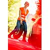 Young female driver wearing a high visibility vest, calling the roadside service/assistance after her car has broken down
