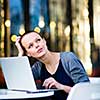 Portrait of a sleek young woman calling on a smartphone and using her laptop in a an
urban/city context (shallow DOF; color toned image)